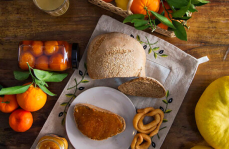 Wooden table with a basket of citrus fruits, rustic bread, plate with bread and jam, juice, jam and buns.