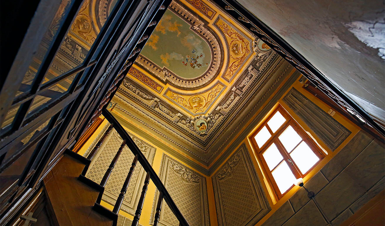 View of painted ceiling and walls with large window from wooden staircase.