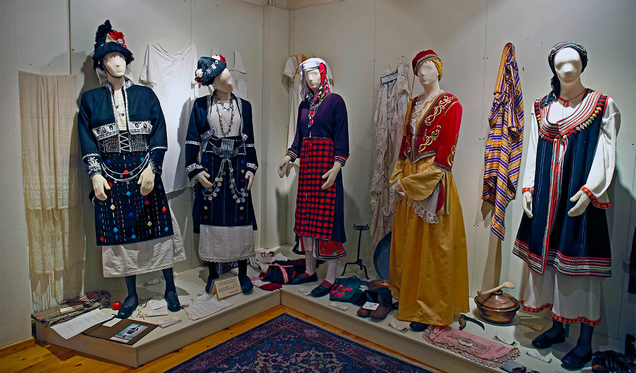 Museum display case with 5 human-sized dolls dressed in traditional costumes.