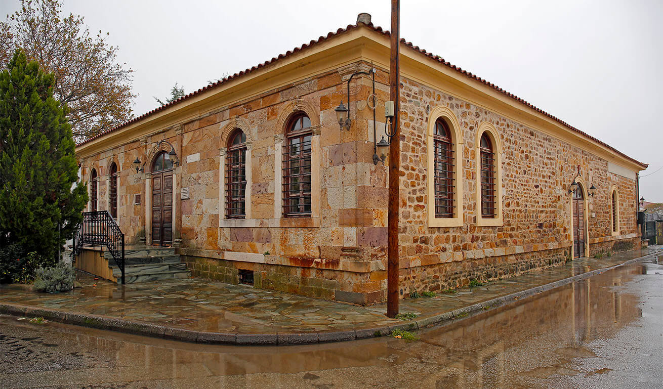 Old ground floor stone building with large arched windows, wooden door and tiles. Rainy winter day.