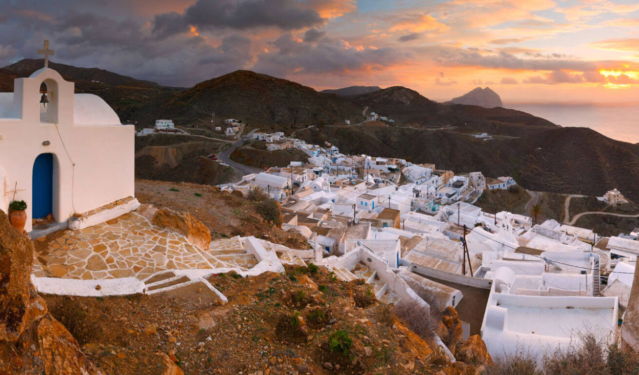 Small white church on top of picturesque settlement in the background dark hills at sunset. 