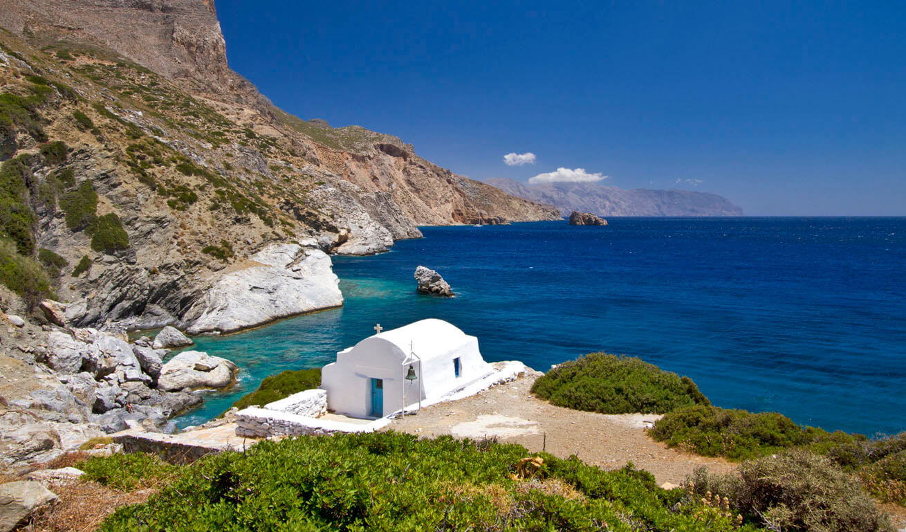 Small white church in front of the sea on rocky shores 