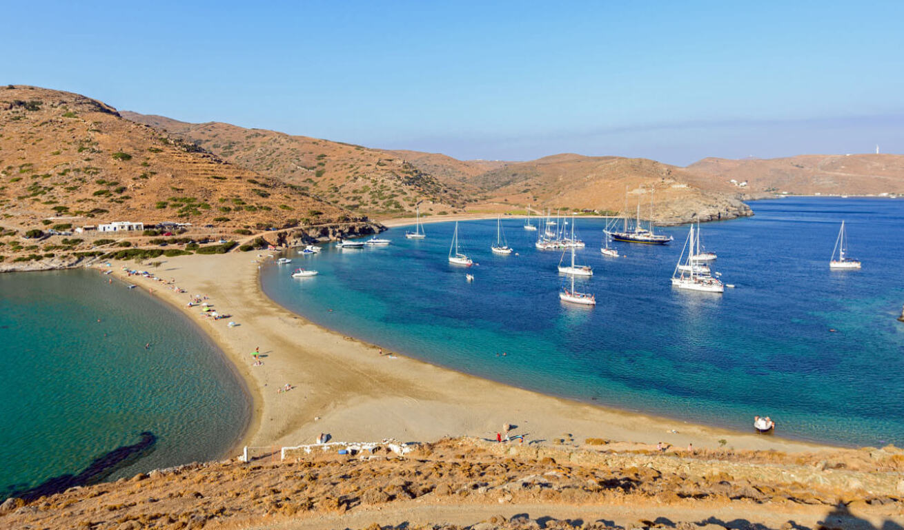 Thin strip of land that forms 2 beaches. Many sailing boats on one and gentle hills with few buildings. 