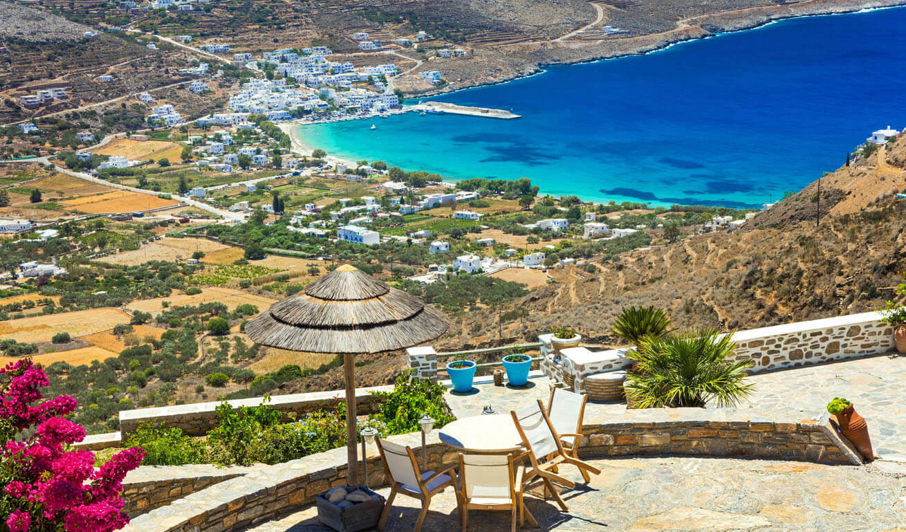 View of a picturesque bay - harbor with white houses. Cycladic landscape. In front a table with chairs under a wooden umbrella.