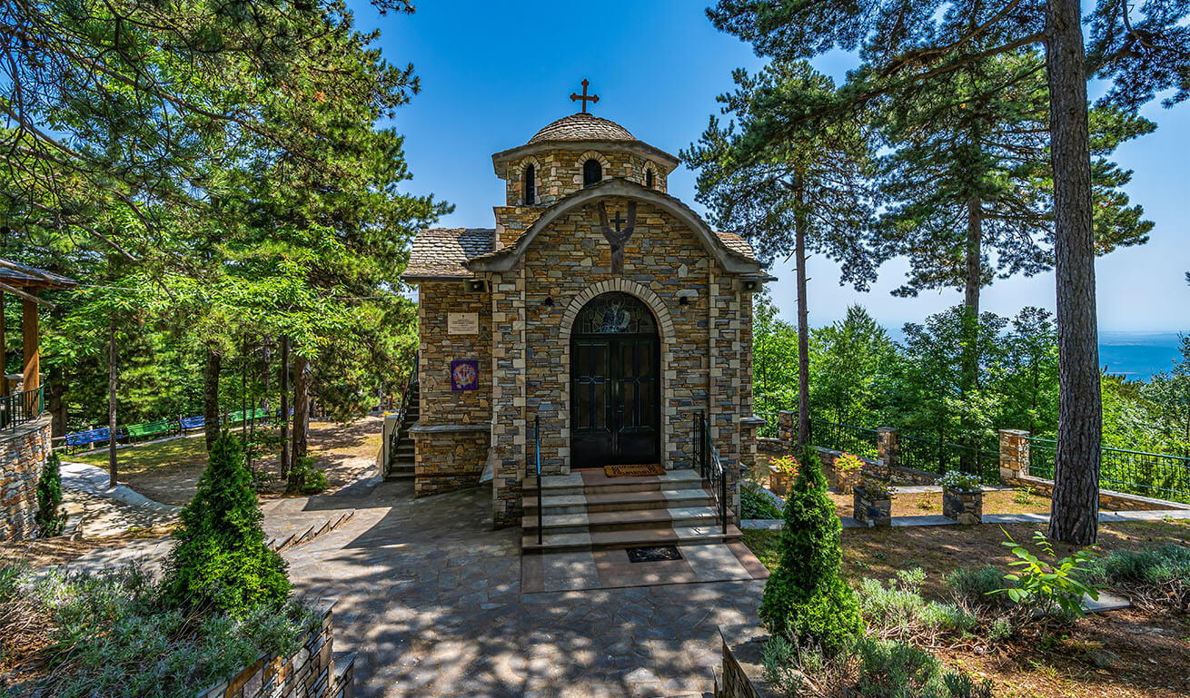 Small stone church with a dome in an outdoor landscaped area with trees. Sunshine.