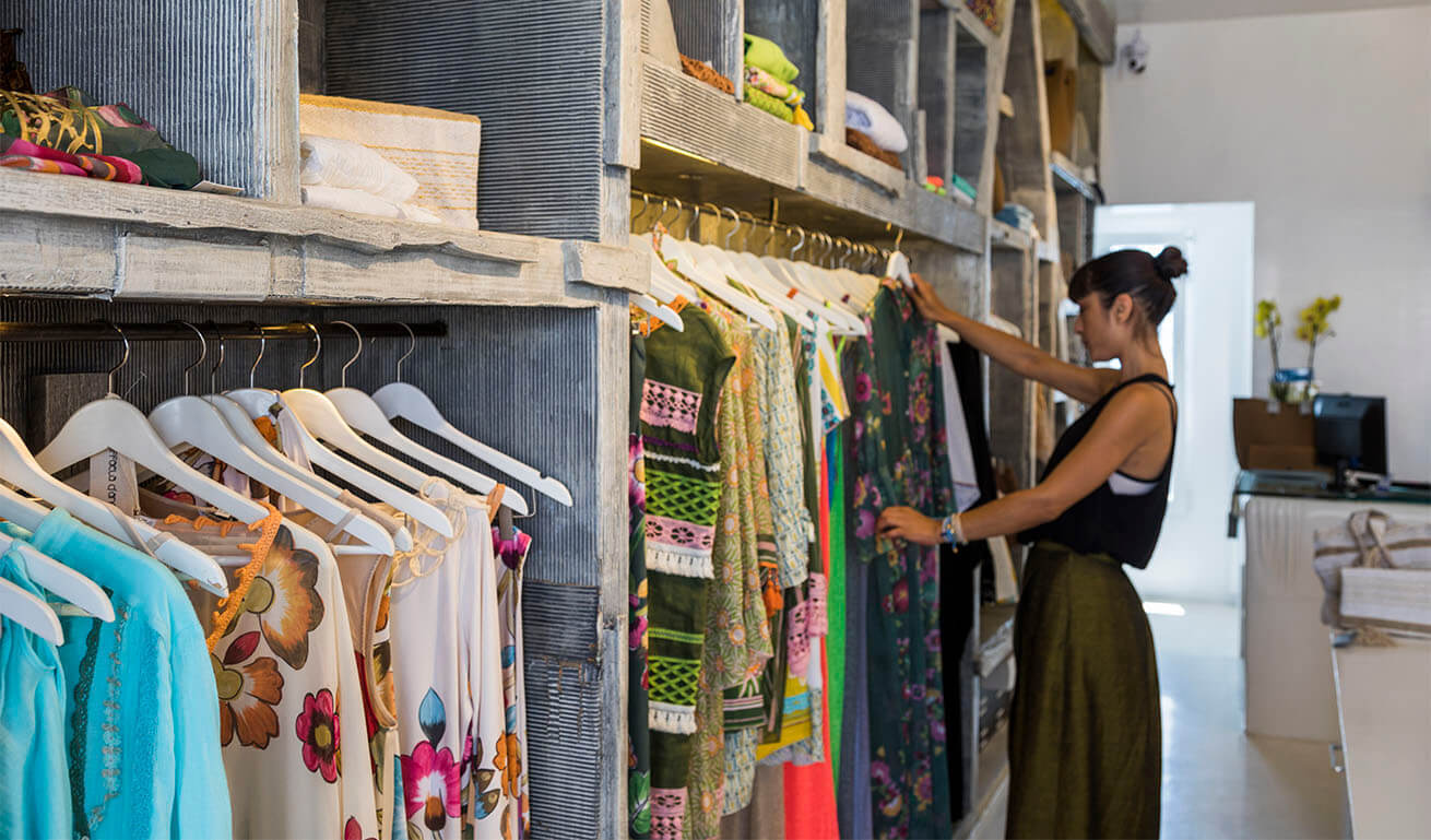 Shop interior with clothes hanging on hangers. A young woman is looking at a dress.