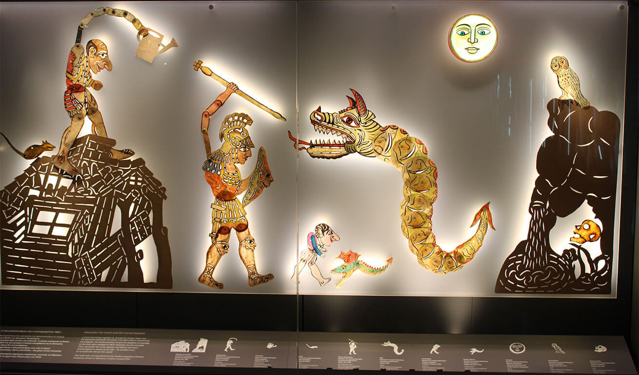 Colored shadow puppet figures in a museum display case.