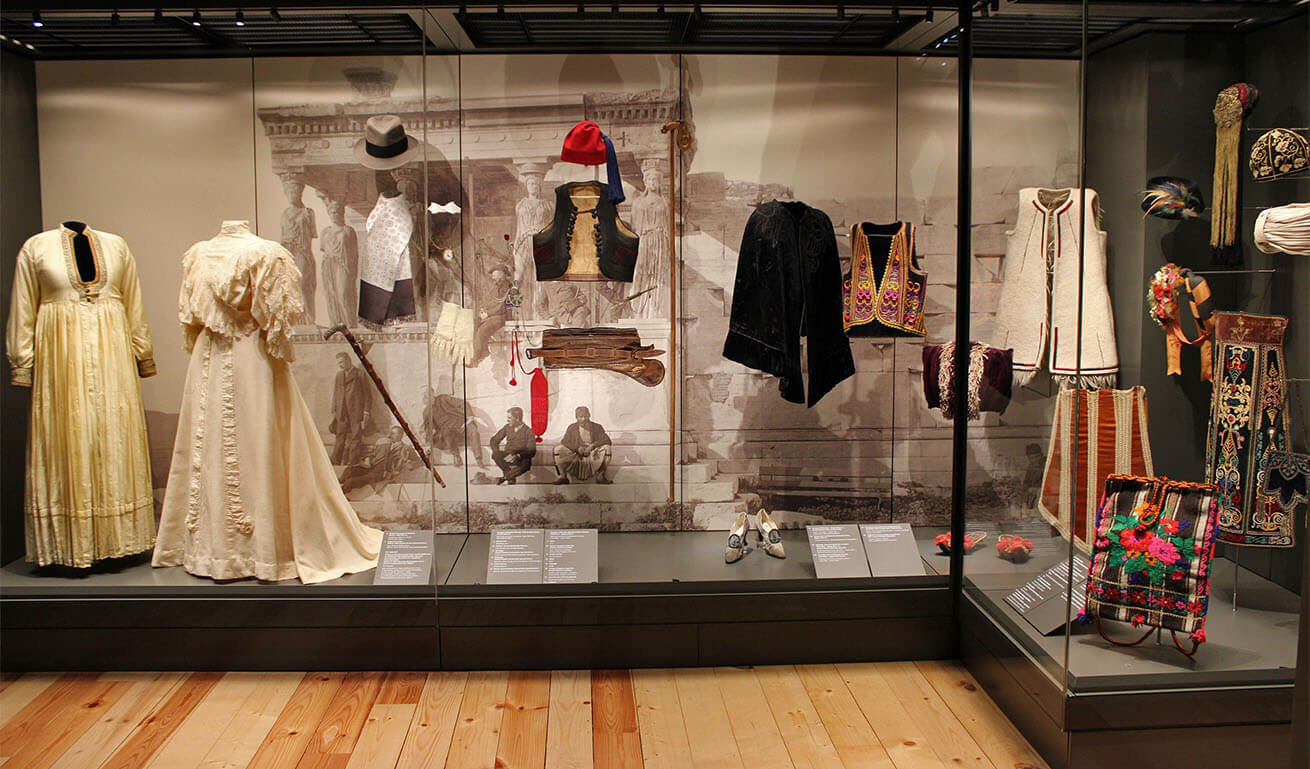 Large glass museum displays with traditional dresses and accessories.