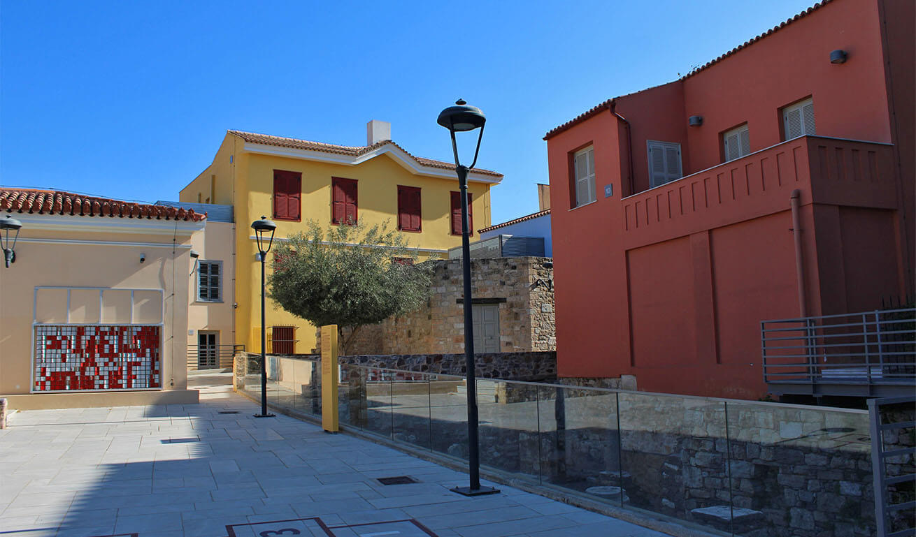 A modern courtyard with colorful buildings, glass railings, and street lamps under a clear blue sky.