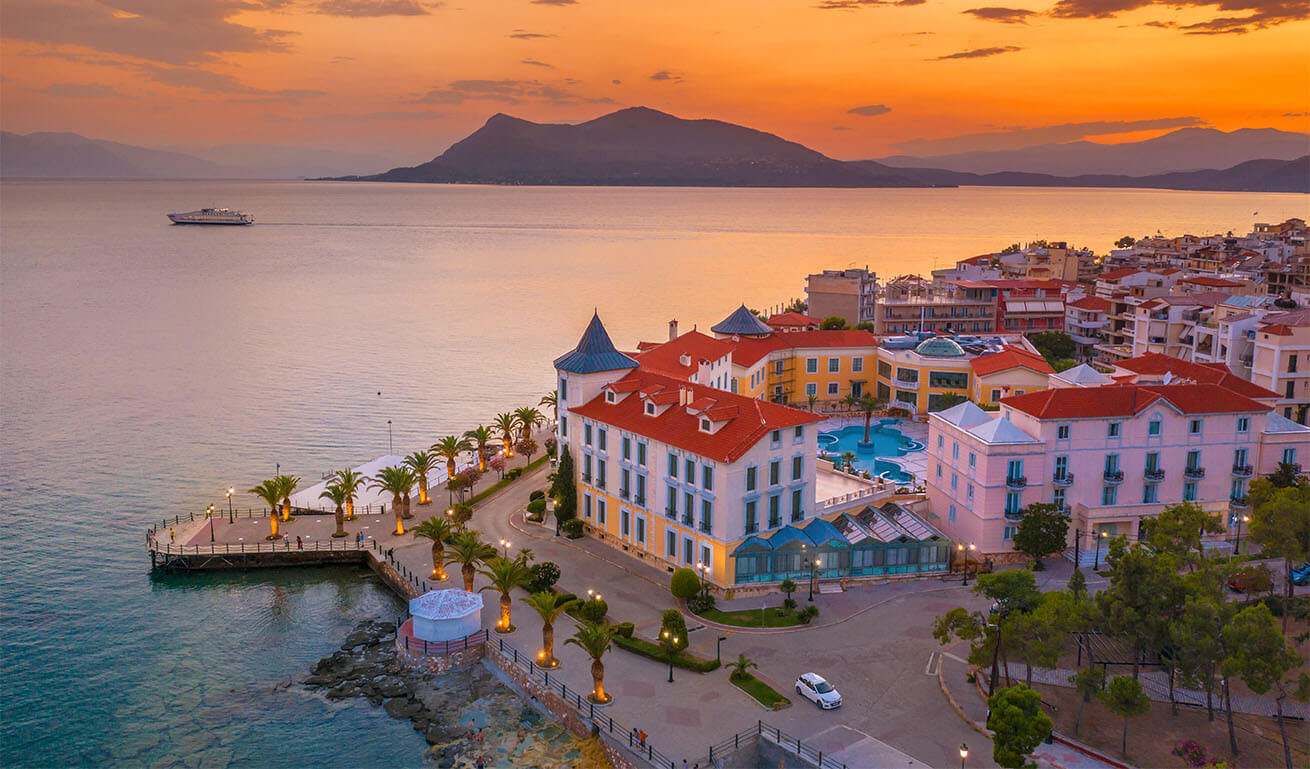 Aerial photograph of a seaside settlement with low-rise, well-preserved buildings with tiles. Waterfront with palm trees and lights. Evening.