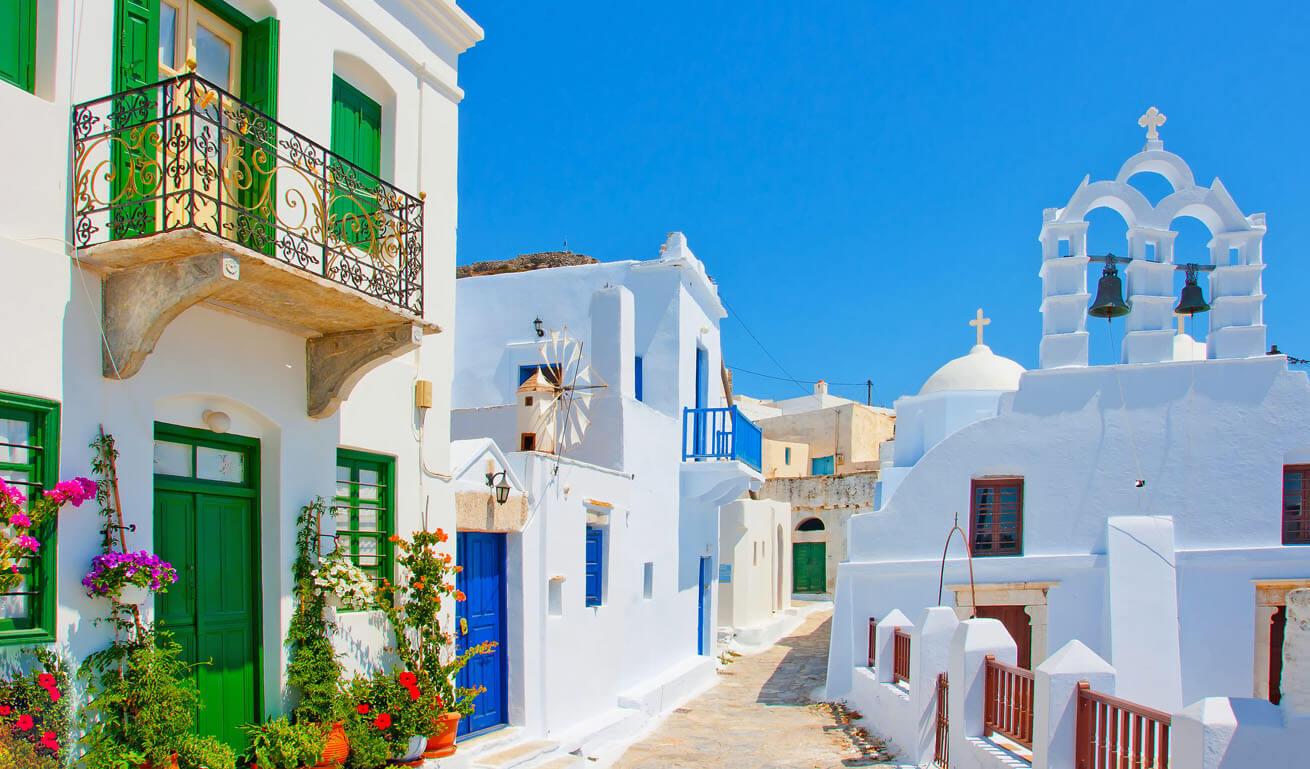 Cycladic cobbled path with white houses and church. Many flower pots at the entrance of a house. 
