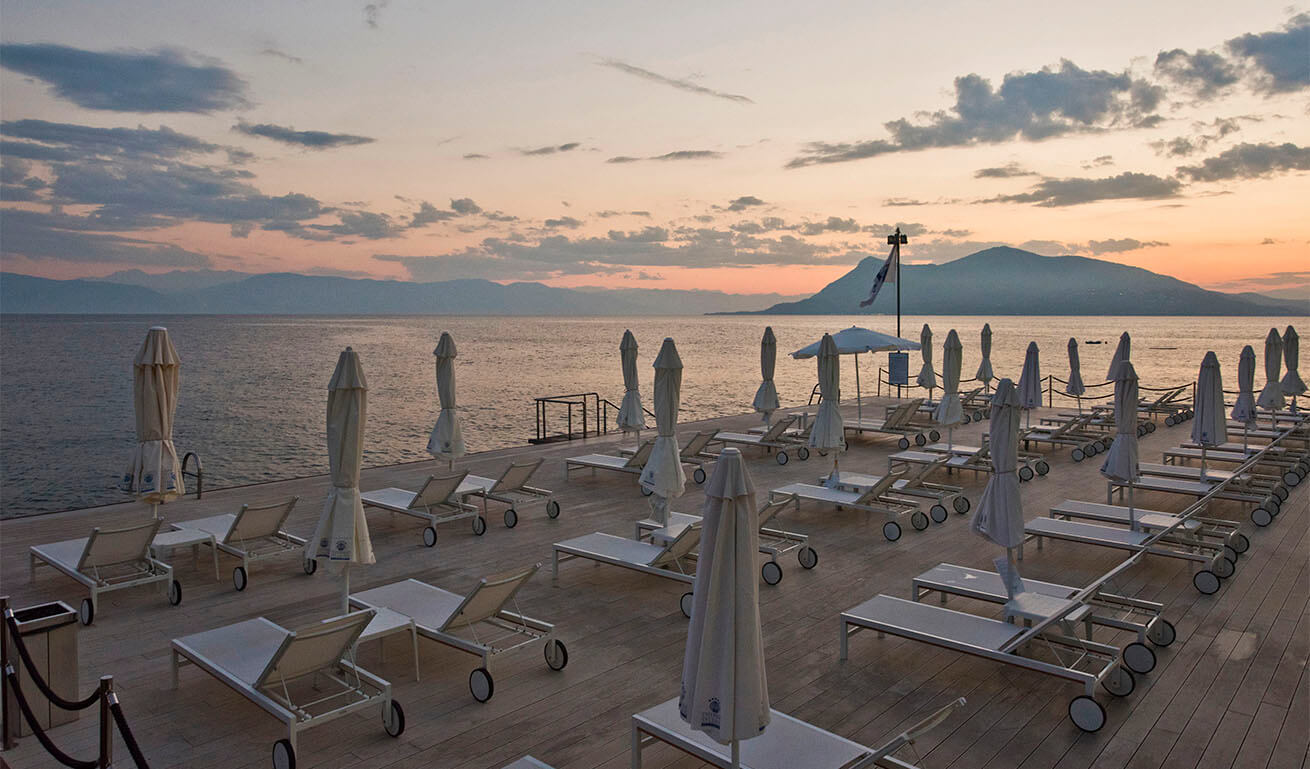 Wooden platform on the waterfront in front of the sea with rows of white sun loungers and closed umbrellas. Evening.