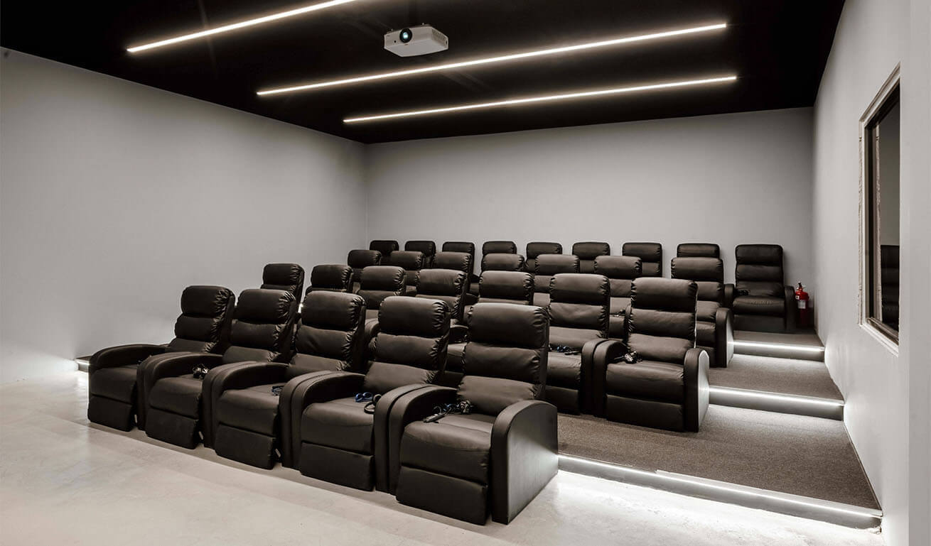 Screening room with black leather armchairs with accessories, light walls and a dark ceiling with a projector.