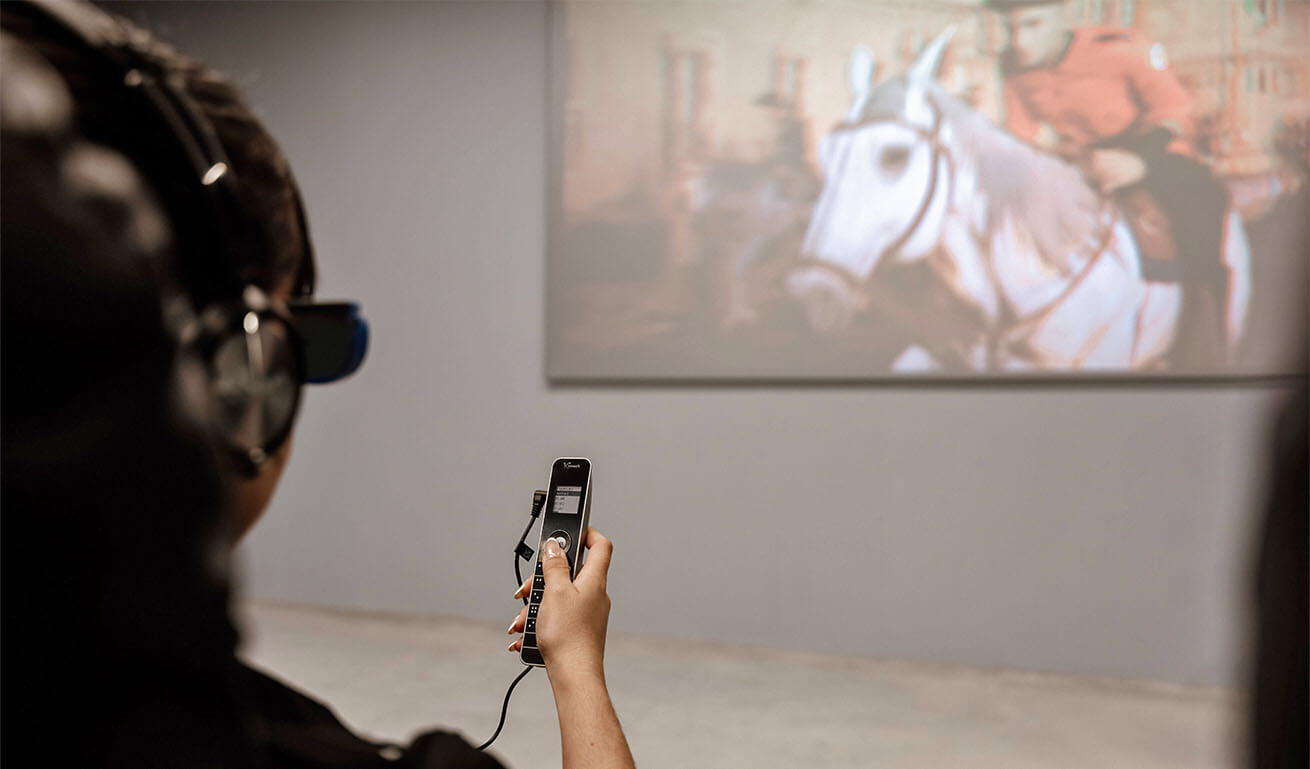 Man with headphones and remote control watching a historical film with a horse and a rider in uniform.
