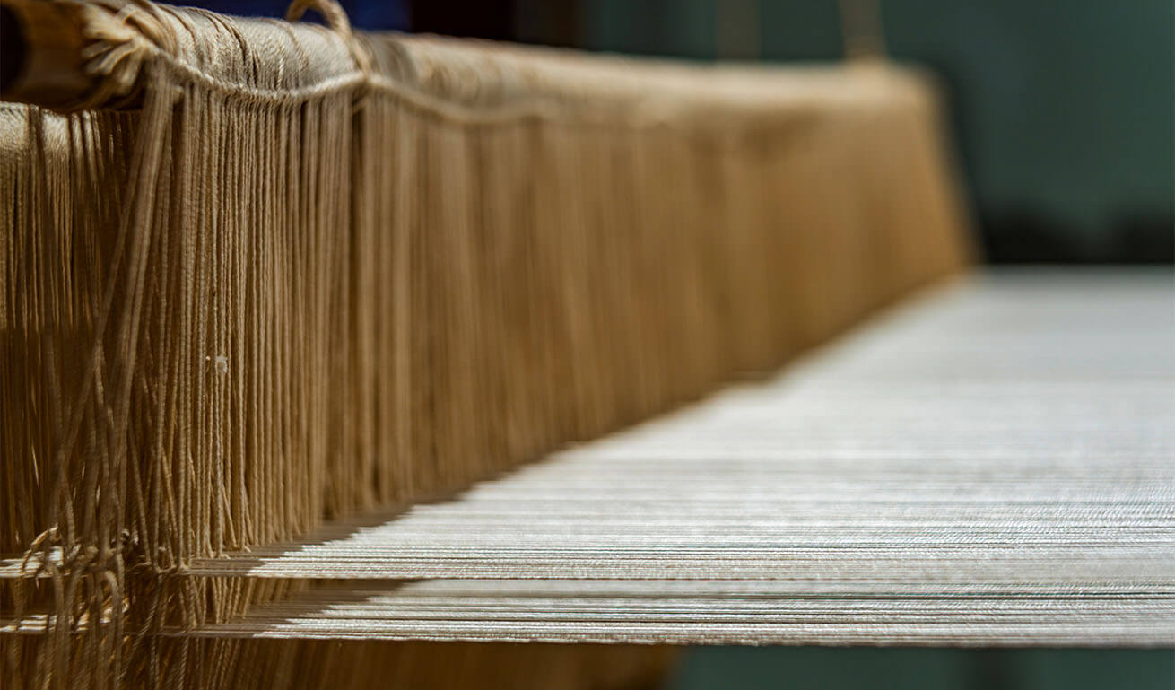Close-up of beige threads on a traditional loom, highlighting their alignment and texture, with a blurred background for depth.