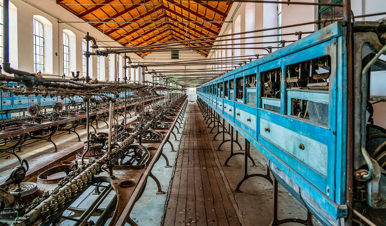 Interior of a historic industrial unit with machinery, a wooden ceiling and large windows that let in plenty of light.