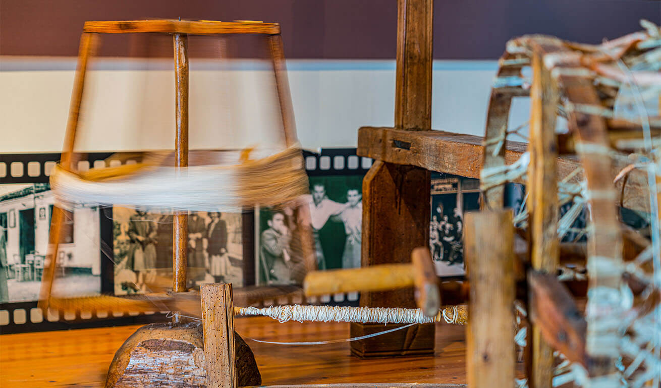 Traditional wooden spinning wheel in motion, with blurred threads and a background of vintage black-and-white photographs depicting cultural scenes.
