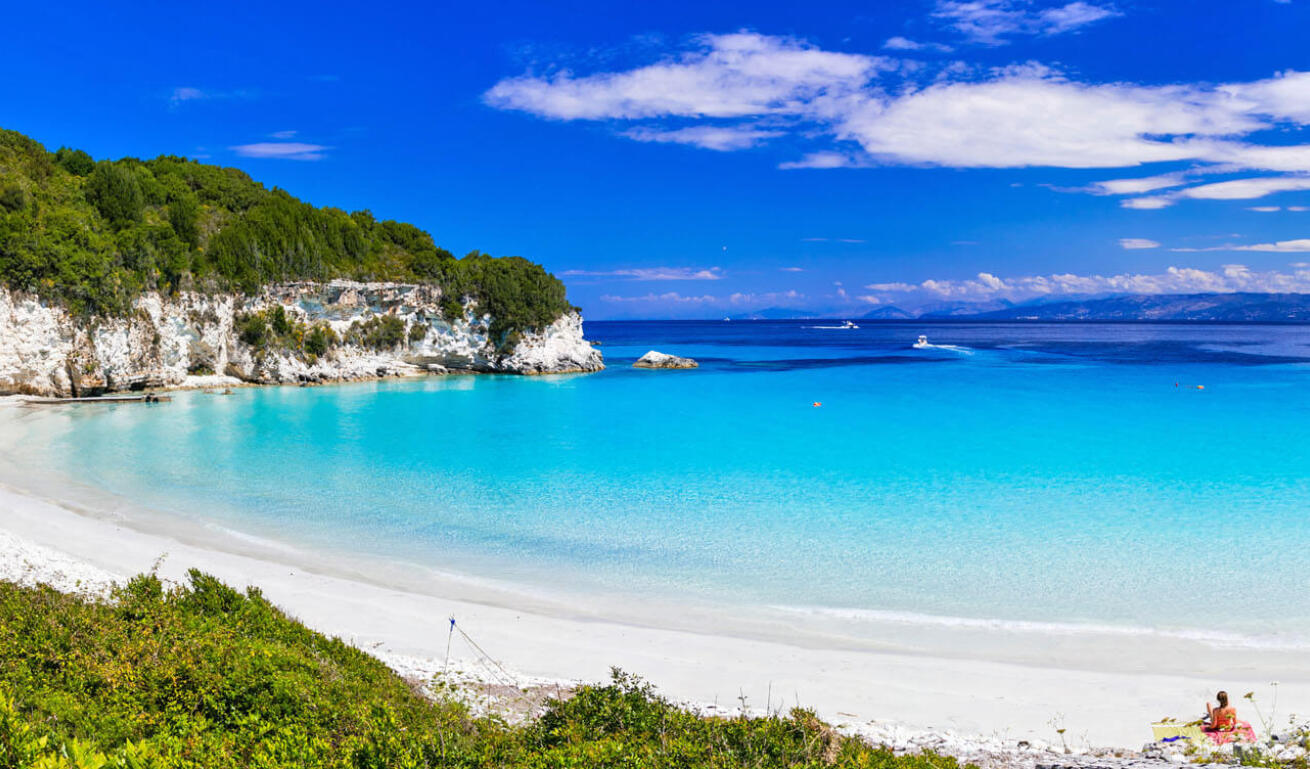 Παραλία Βουτούμι με γαλαζοπράσινα νερά και λίγους λουόμενους και στο βάθος σκάφη