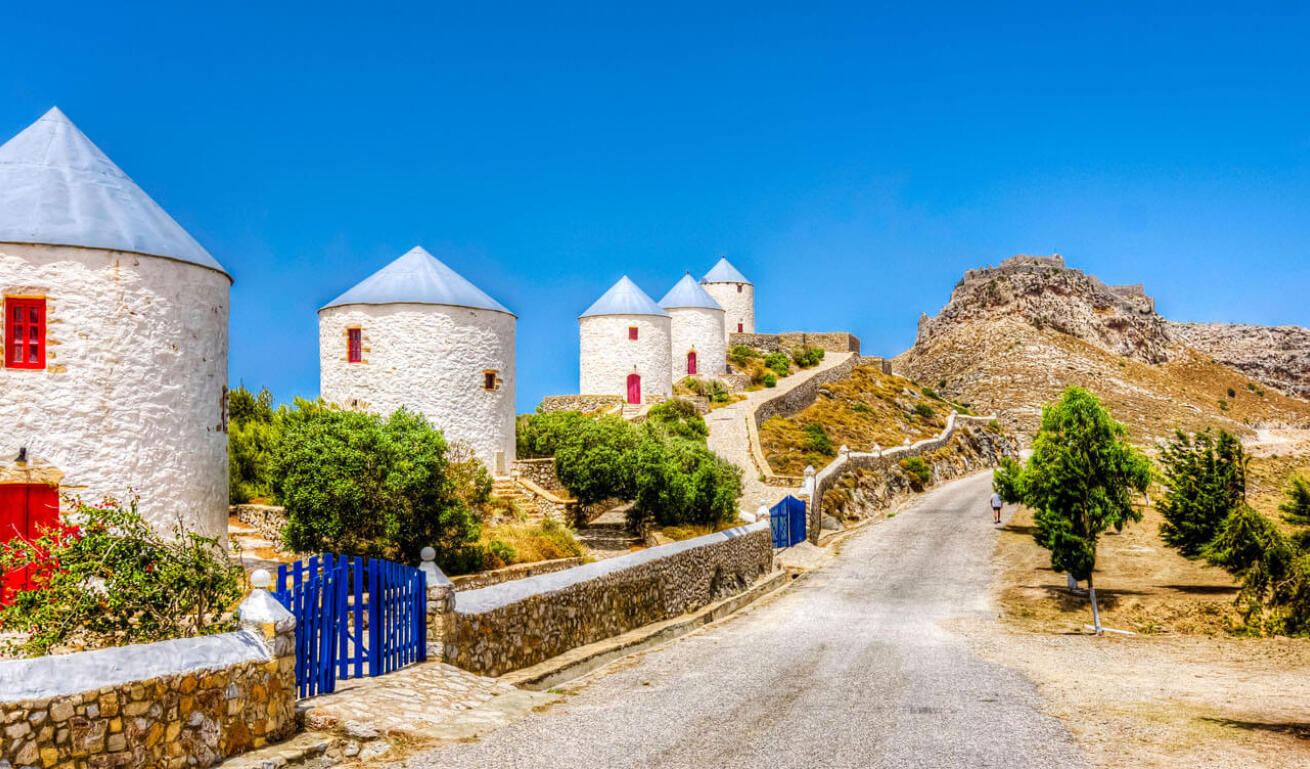 Whitewashed houses with blue rooftops and red doors and windows bulit as windmills along the road