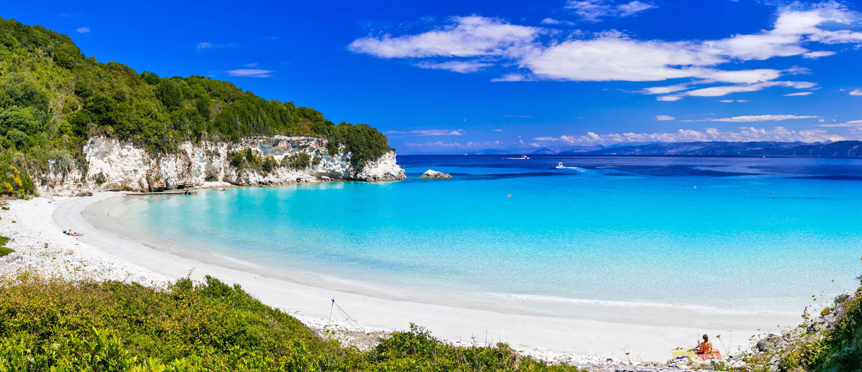 Voutoumi beach with greenish blue waters and a few people hanging around and boats in the background