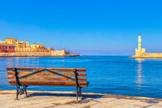 Παγκάκι με θέα θάλασσα. Από τη μια πλευρά παραδοσιακά χρωματιστά κτίρια και πέτρινα τείχη και από την άλλη πέτρινος φάρος.