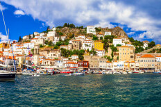 Μεγάλα πέτρινα σπίτια χτισμένα σε πλαγιά λόφου που καταλήγει σε προκυμαία με μικρά σκάφη.