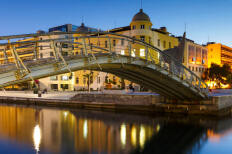 Προκυμαία και μεταλική γέφυρα το δειλινό με αναμμένα φώτα.