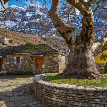Winter view of Papigo village, with a stone built house under a tall mountain.