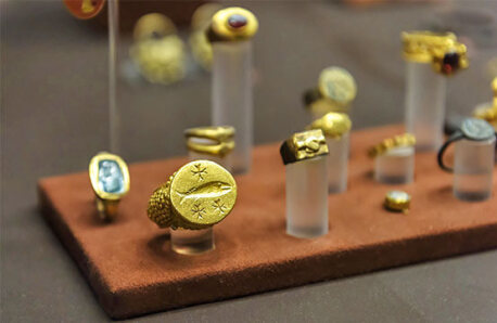 Gold jewelry in a museum display case. The first ring depicts a fish and 3 crosses.