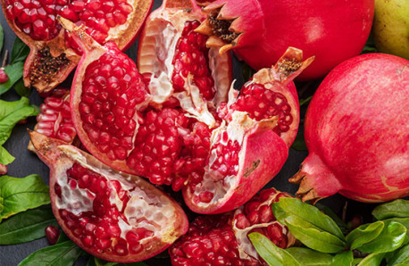Red pomegranates, whole and opened on a surface with a few green leaves.