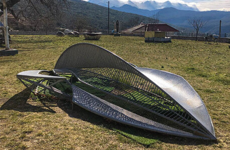 Outdoor area with grass and modern sculptures. Winter and sunshine. In the background small house with tiles and landscape with mountains.