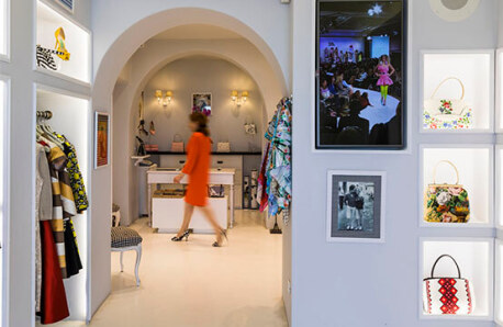 Interior of a clothing and accessories store. Arches and a woman in a red dress walking in the background.