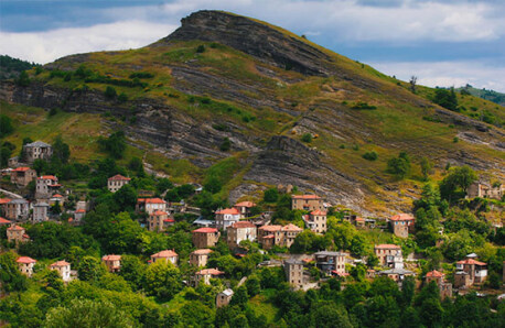Traditional settlement on low mountain slope with green trees.