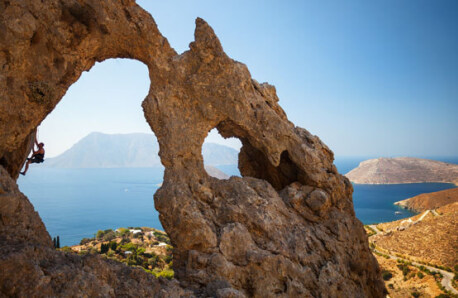 Απότομος βράχος με 2 μεγάλες τρύπες. Πίσω τους φαίνεται στεριά, θάλασσα και νησιά. Άντρας σκαρφαλώνει στην μεγαλύτερη τρύπα.