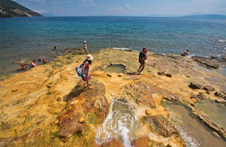 Seaside landscape with low rocks in yellowish colors next to the sea with few people. Sunny summer day.