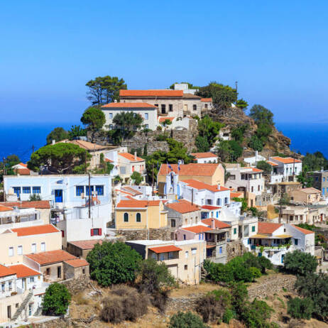 Picturesque settlement at the top of a hill. Tiled houses with some trees in between. In the background is the sea. 
