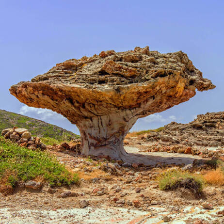 Mushroom-shaped rock in a rocky landscape with low green vegetation. 