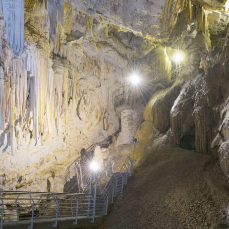 Interior of a large cave with stalactites and a corridor for visitors with lights. 