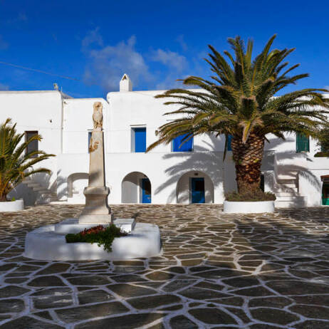 Paved square with a column, palm tree and white houses with arches. 