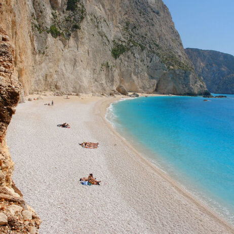 Lefkada beach with greenish blue waters between the steep rocks and with people hanging around