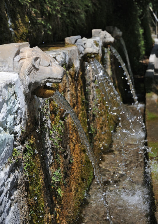 Low stone wall with 3 lion heads from which water runs and ends in a small channel 