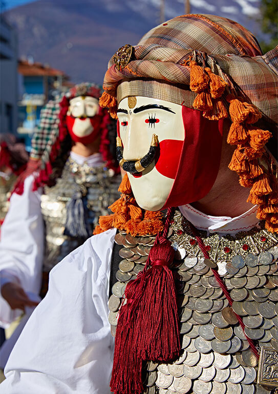 Men wearing masks and traditional costumes and elaborate headscarves in a sunny city. Close-up of the mask and the coins of the costume.