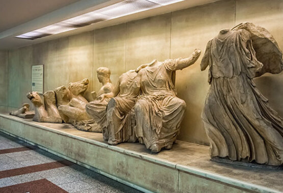 Replicas of ancient statues from the Parthenon frieze in a display case.