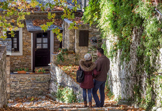 Couple walking on cobbled street between traditional stone houses and plants.