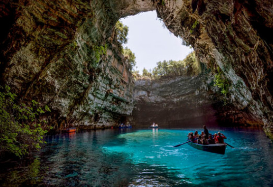 Cave with turquoise waters and an opening at the top where the sky and trees can be seen. Boats with people on the water.