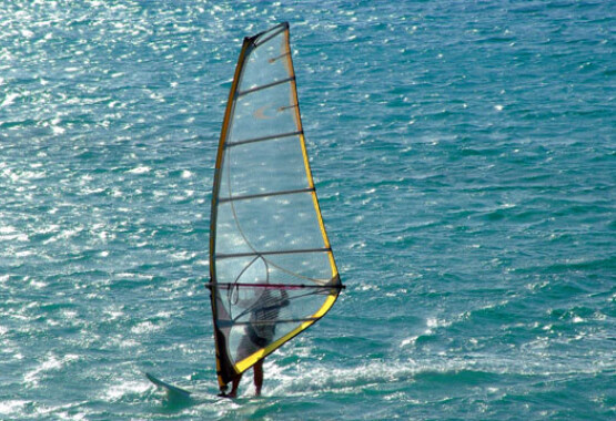 Ένας windsurfer πλέει στην σκούρα γαλάζια θάλασσα κόντρα στον ήλιο.