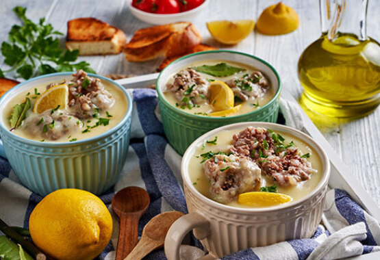 Bowls filled with soup on a table cloth with a bottle of olive oil and lemon on the side.