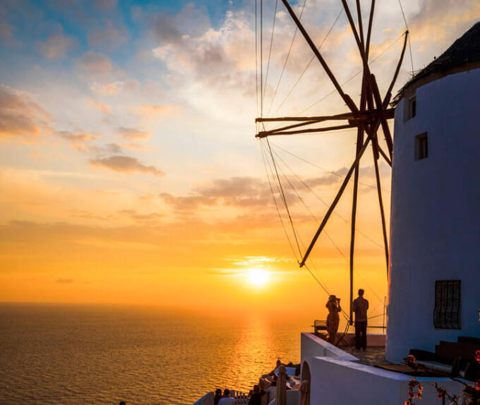 Ανεμόμυλος και λίγοι άνθρωποι με φόντο ηλιοβασίλεμα.