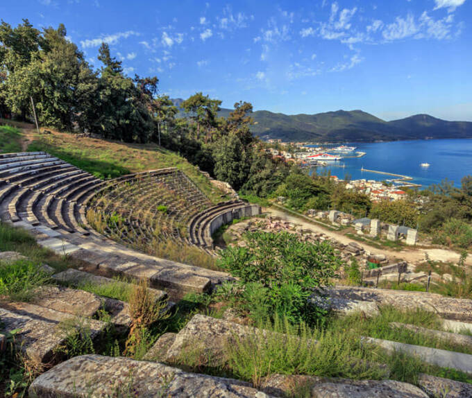 Αρχαίο θέατρο και στο βάθος αχνοφαίνεται χωριό και η θάλασσα