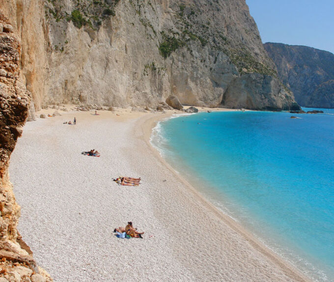 Παραλία της Λυκάδας με γαλαζοπράσινα νερά ανάμεσα στα ψηλά βράχια και με λουόμενους τριγύρω